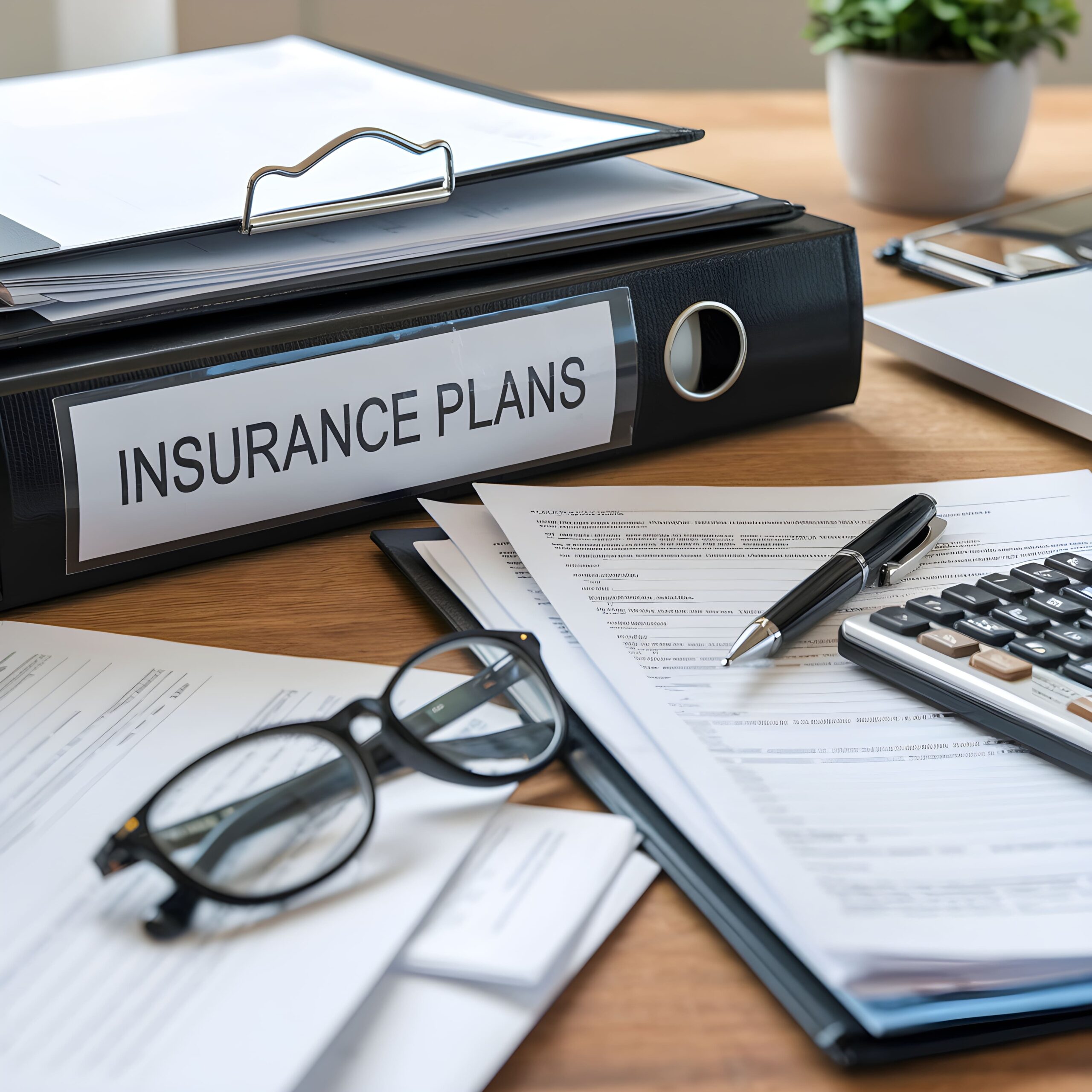desk-with-binder-labeled-insurance-plans-glasses-pen-calculator-scattered-papers